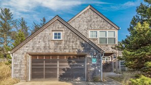 A two-story house with a garage, a small window on the first floor, and a larger window on the second floor. - Delightfully Decorated Home Walking Distance to the Beach, Fireplace, Deck, BBQ (Pacific City)