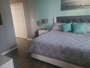 A bedroom with a patterned bedspread, a nightstand with a lamp, and a door in the background.