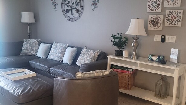 A living room with a sofa, ottoman, and a console table with decorative items. - Affordable, One floor, Spacious Condo, Conveniently Located 15 minutes to Disney (Kissimmee)