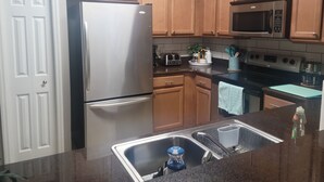 A kitchen with wooden cabinets, a stainless steel refrigerator, a microwave, a stove, and a sink. - Affordable, One floor, Spacious Condo, Conveniently Located 15 minutes to Disney (Kissimmee)