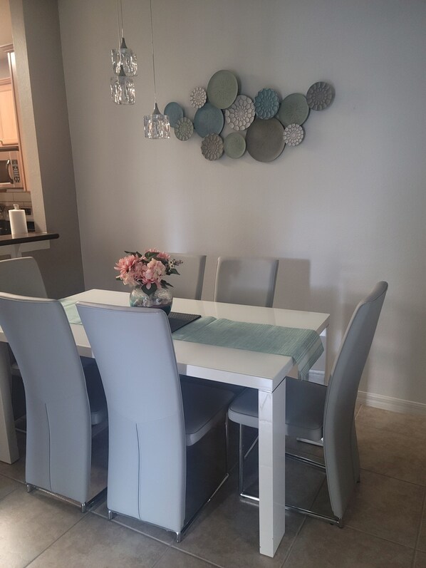 A dining area with a white table, grey chairs, a vase with flowers, and decorative wall art.