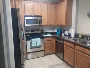 A kitchen with wooden cabinets, a stainless steel refrigerator, a microwave, a stove, a coffee maker, and a sink.
