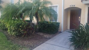 A building with a number 2744 on the door, surrounded by greenery and a paved walkway. - Affordable, One floor, Spacious Condo, Conveniently Located 15 minutes to Disney (Kissimmee)