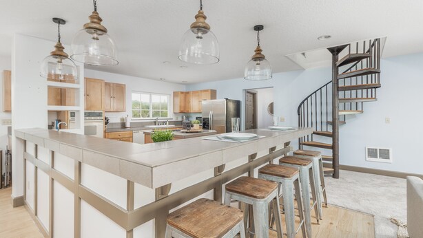 Une cuisine moderne dotée d’un îlot central, de tabourets de bar, d’appareils électroménagers en acier inoxydable, de meubles de rangement en bois et d’un escalier en colimaçon.