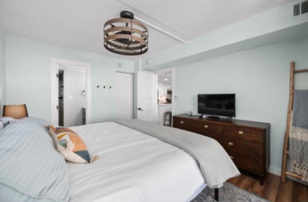 Une chambre à coucher comprenant un lit, une commode, un téléviseur et un luminaire fixé au plafond.