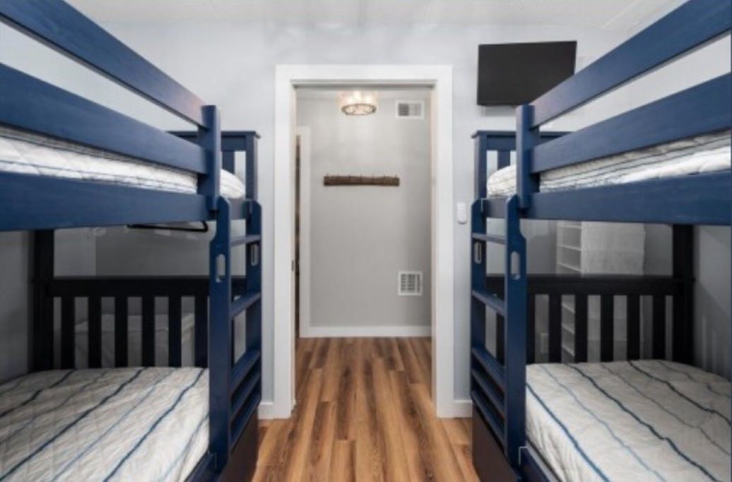 A narrow hallway with bunk beds on either side, a door at the end, and a light fixture on the ceiling.