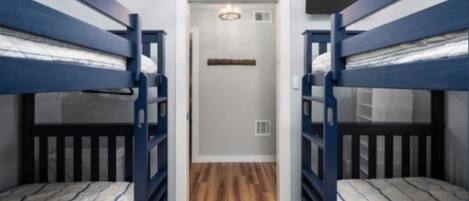 A narrow hallway with bunk beds on either side, a door at the end, and a light fixture on the ceiling.