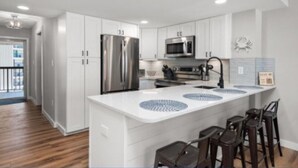 A modern kitchen with white cabinets, stainless steel appliances, and a bar area with stools.