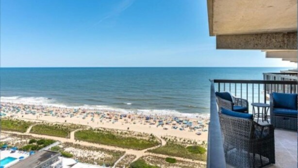A balcony with wicker furniture overlooking a beach with umbrellas and people.