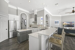 A modern kitchen with a central island, stainless steel appliances, and a dining area with a TV. - Sea of Dreams. Remodeled Lakefront 4 Bed, Heated Pool, Golf Cart and Bikes! (Destin)