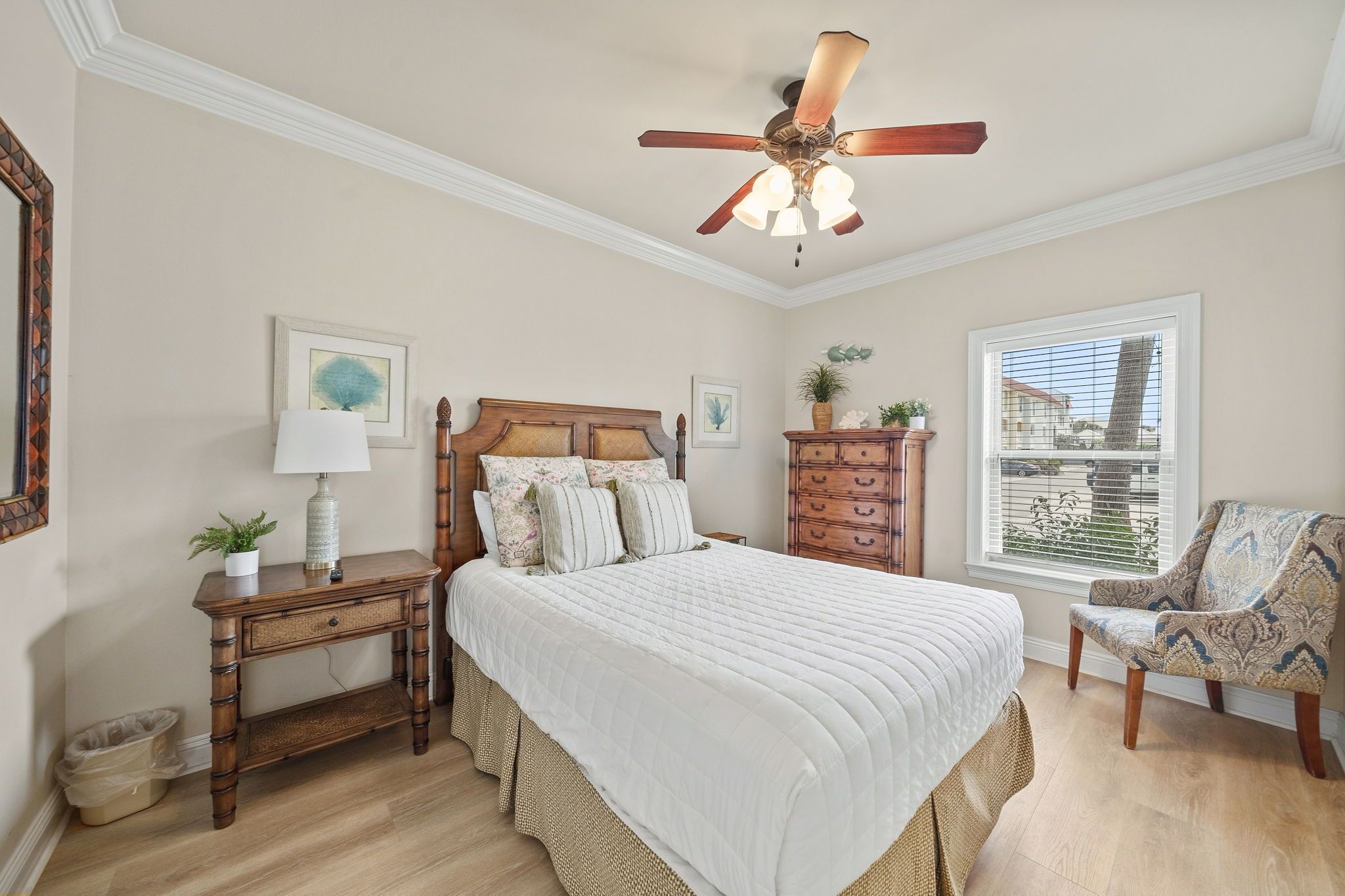 Un dormitorio con cama, mesita de noche, silla, cómoda, ventilador de techo y ventana con persianas.