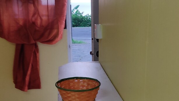 Ein Zimmer mit einem weißen Tisch, einem Korb, einem roten Vorhang und Blick ins Freie.