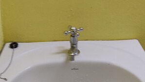 Ein weißes Waschtuch mit einem einzelnen Wasserhahn vor einer gelben Wand.