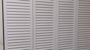 Ein weißer Schrank mit horizontalen Lamellen und zwei Griffen.