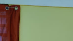 Ein Bett mit einem roten Gegenstand darauf, einem braunen Vorhang und einer grünen Wand.