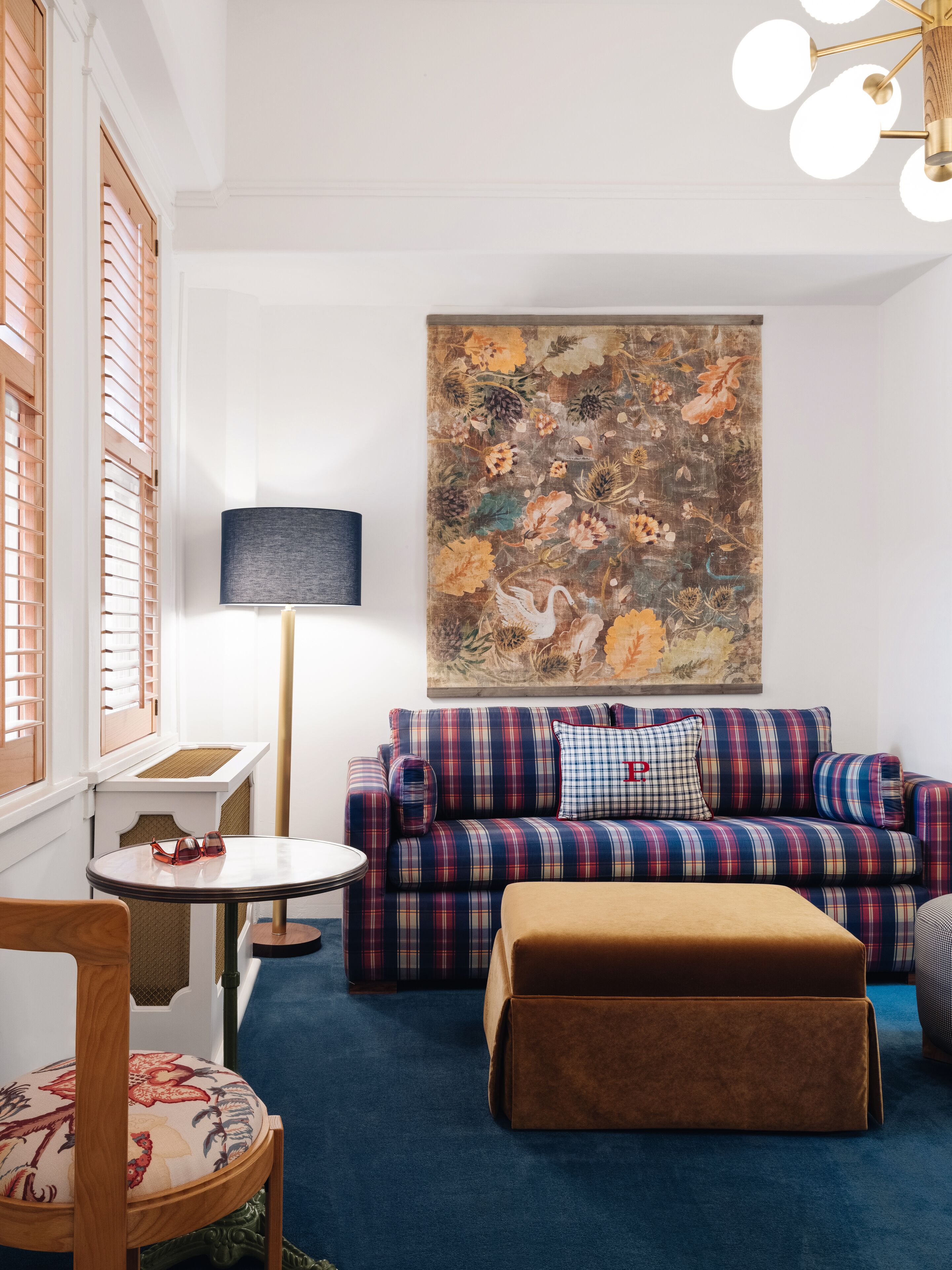 Un salon chaleureux avec un canapé à carreaux, une table ronde et un grand tableau floral accroché au mur.
