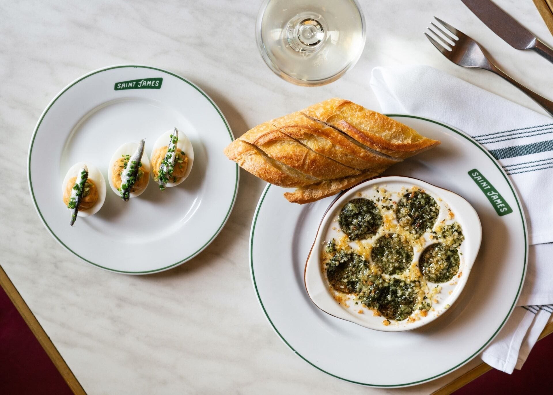 Une table à manger avec des assiettes remplies de nourriture, un verre d’eau et des couverts.