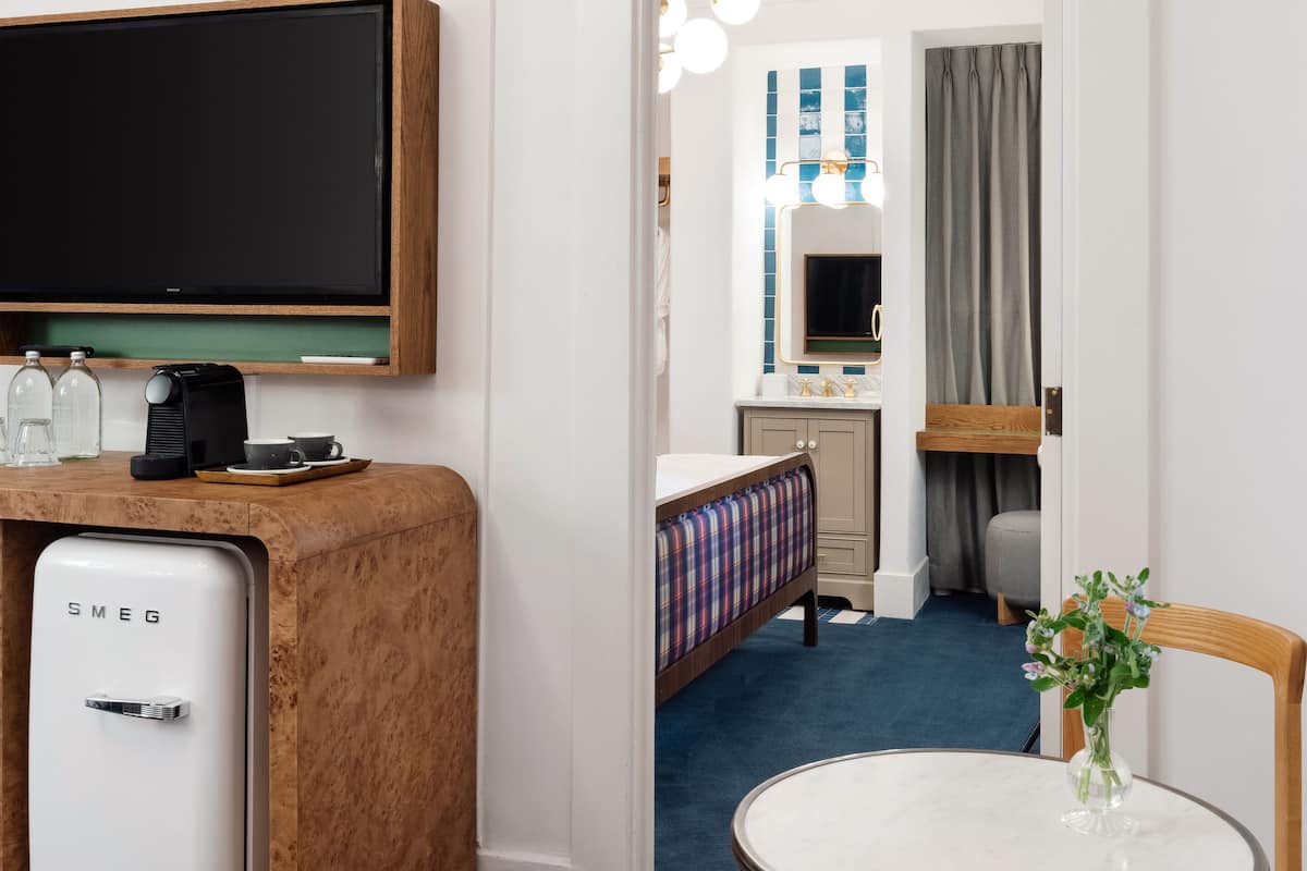 Ein Hotelzimmer mit Fernseher, Minibar und einem kleinen Tisch mit einer Vase.