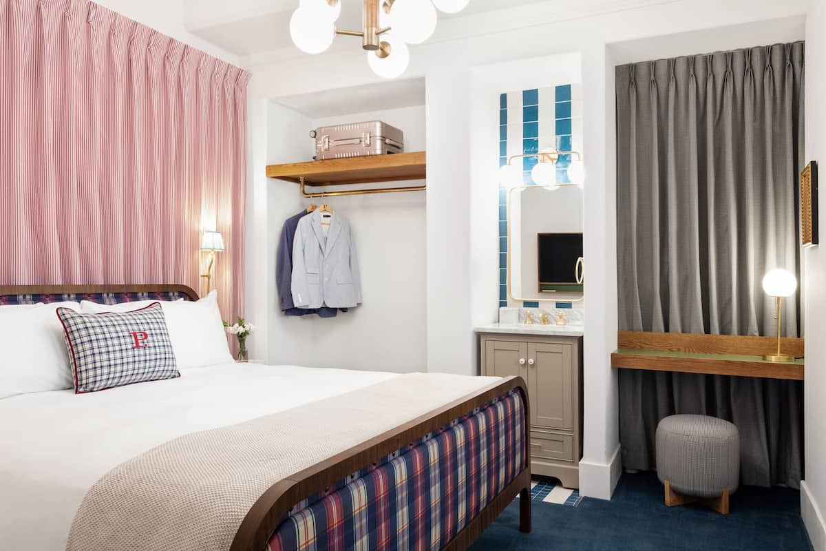 Ein ordentlich eingerichtetes Schlafzimmer mit Bett, Nachttisch, Lampe und einem kleinen Hocker.