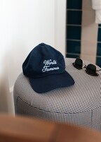 A navy blue cap with "World Famous" embroidered on it, placed on a checkered ottoman next to a pair of sunglasses.