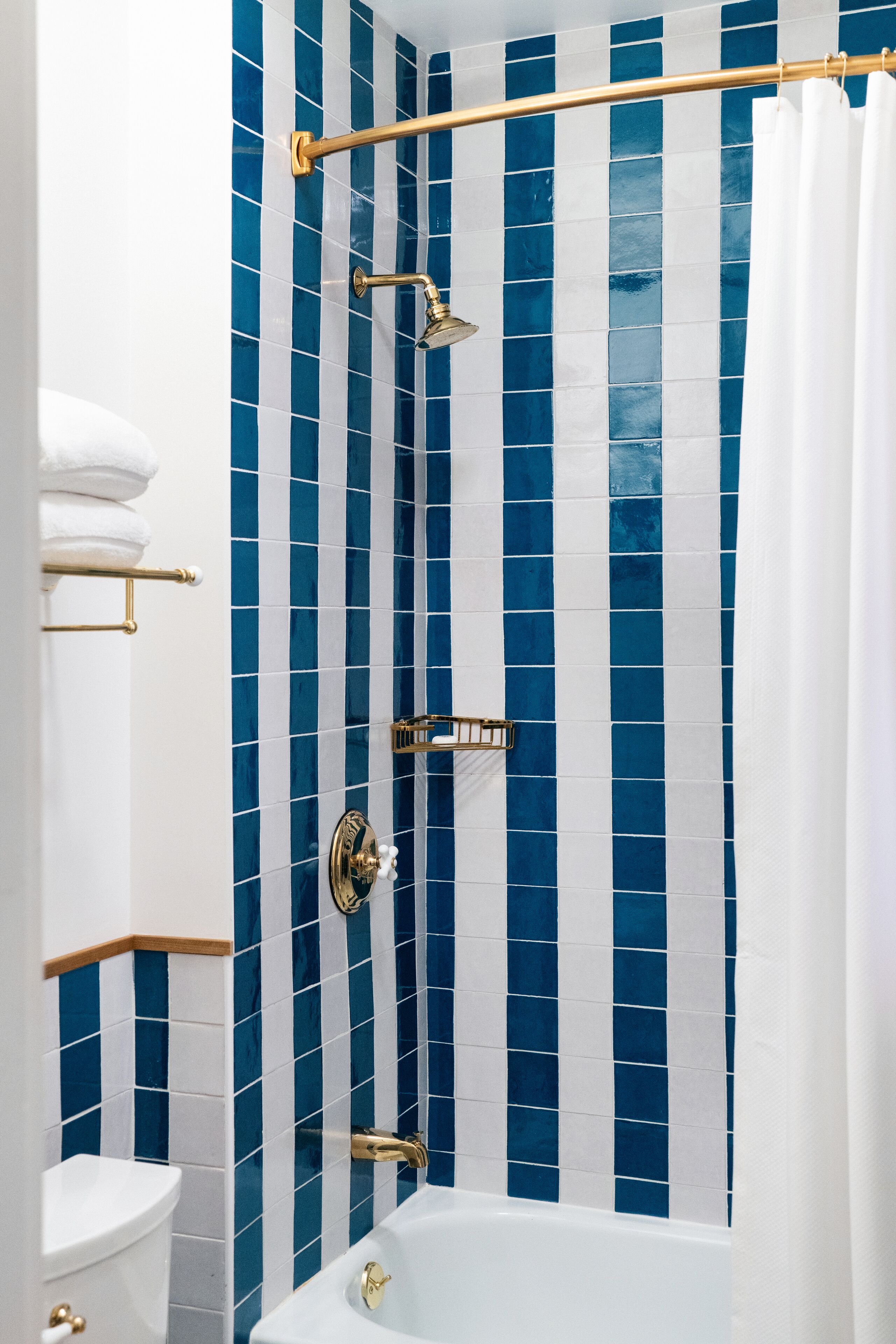 A bathroom with a white bathtub, a shower with a gold showerhead, and a blue and white striped tile wall.