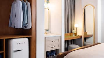 A hotel room with a wardrobe, a bed, a bathroom with a mirror, and a small refrigerator.