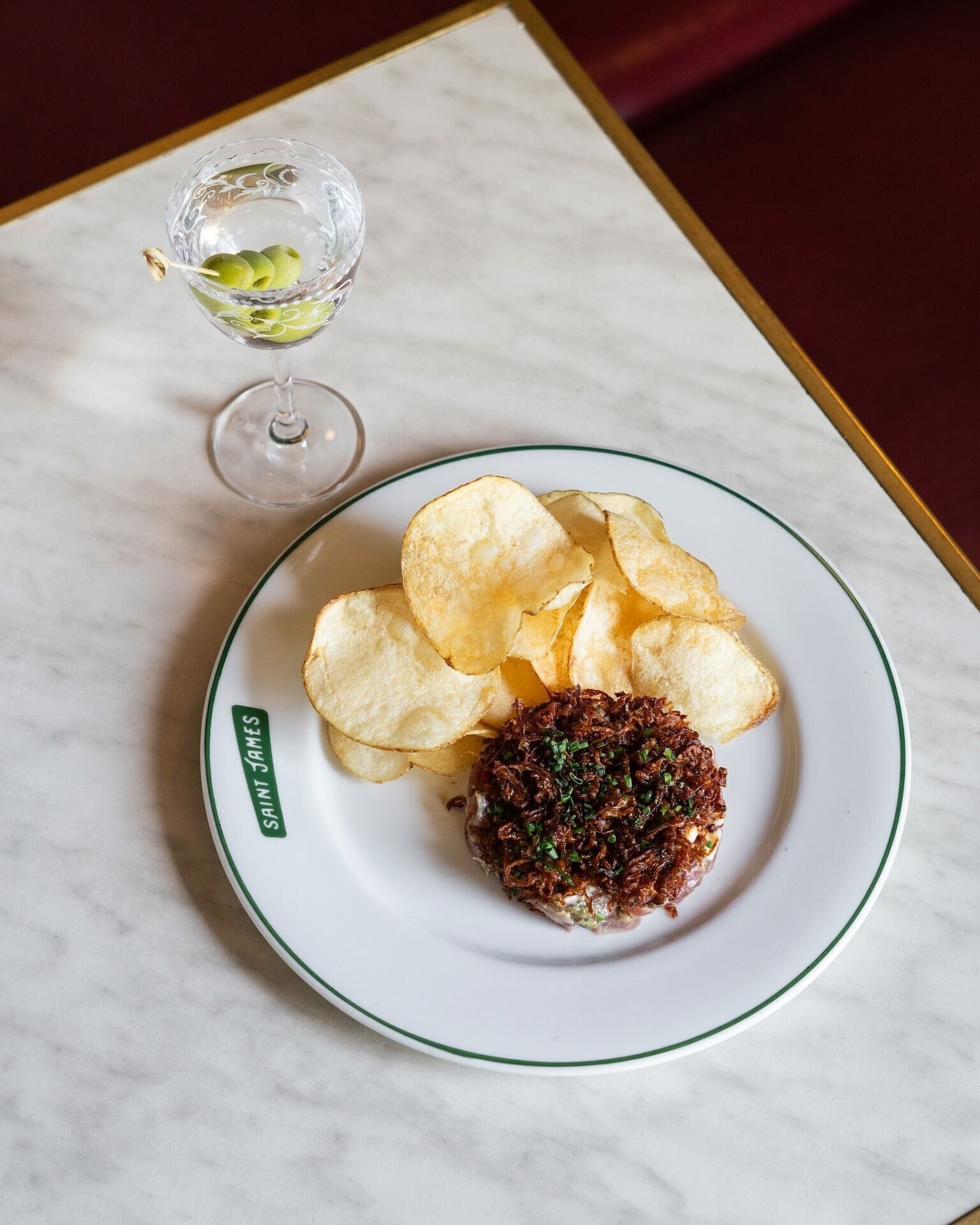 A plate with chips and a meat dish, a glass with a drink, and a marble table.