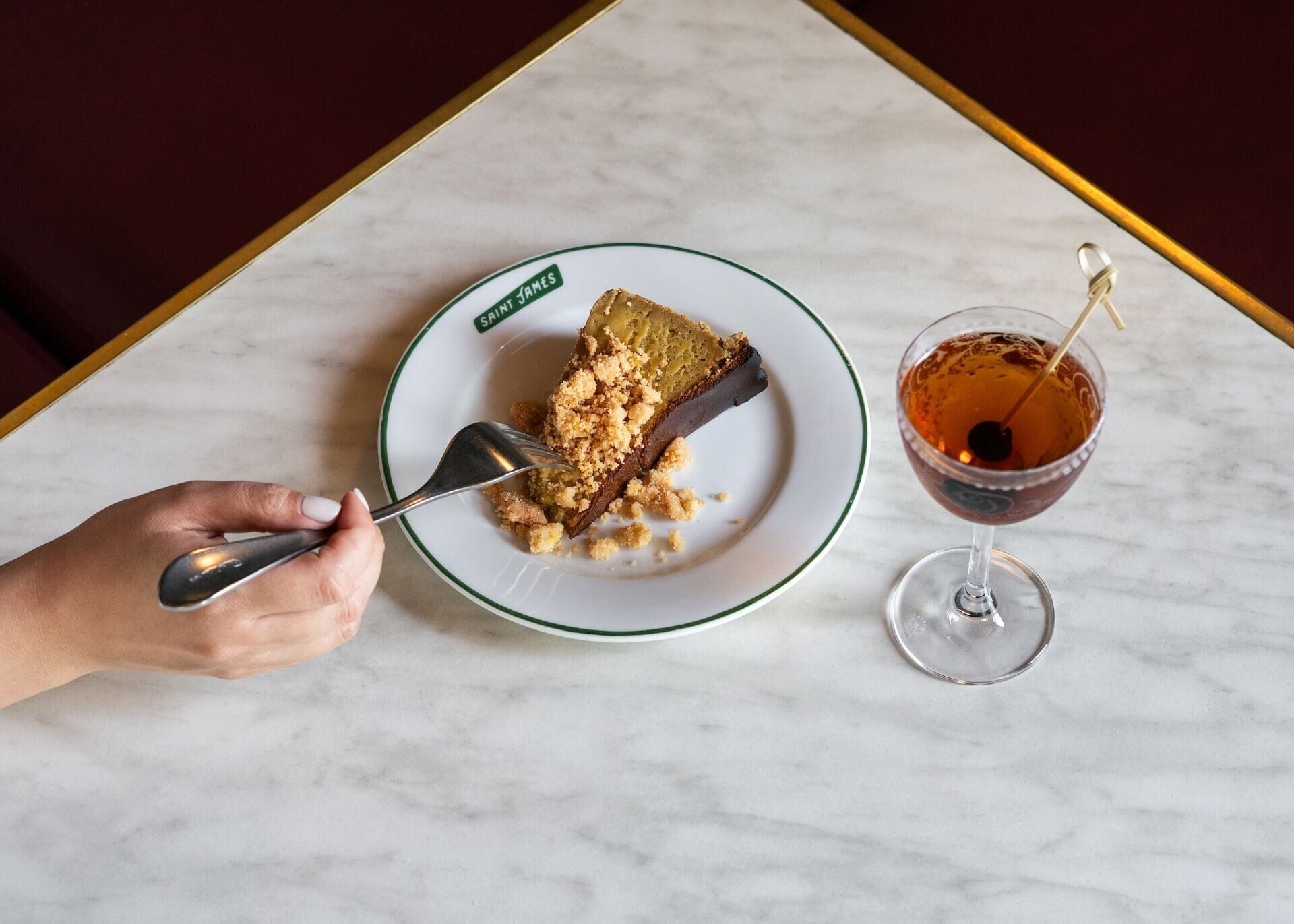 Uma fatia de torta com migalhas em um prato com a inscrição 'SAINT JAMES' sobre uma mesa de mármore.