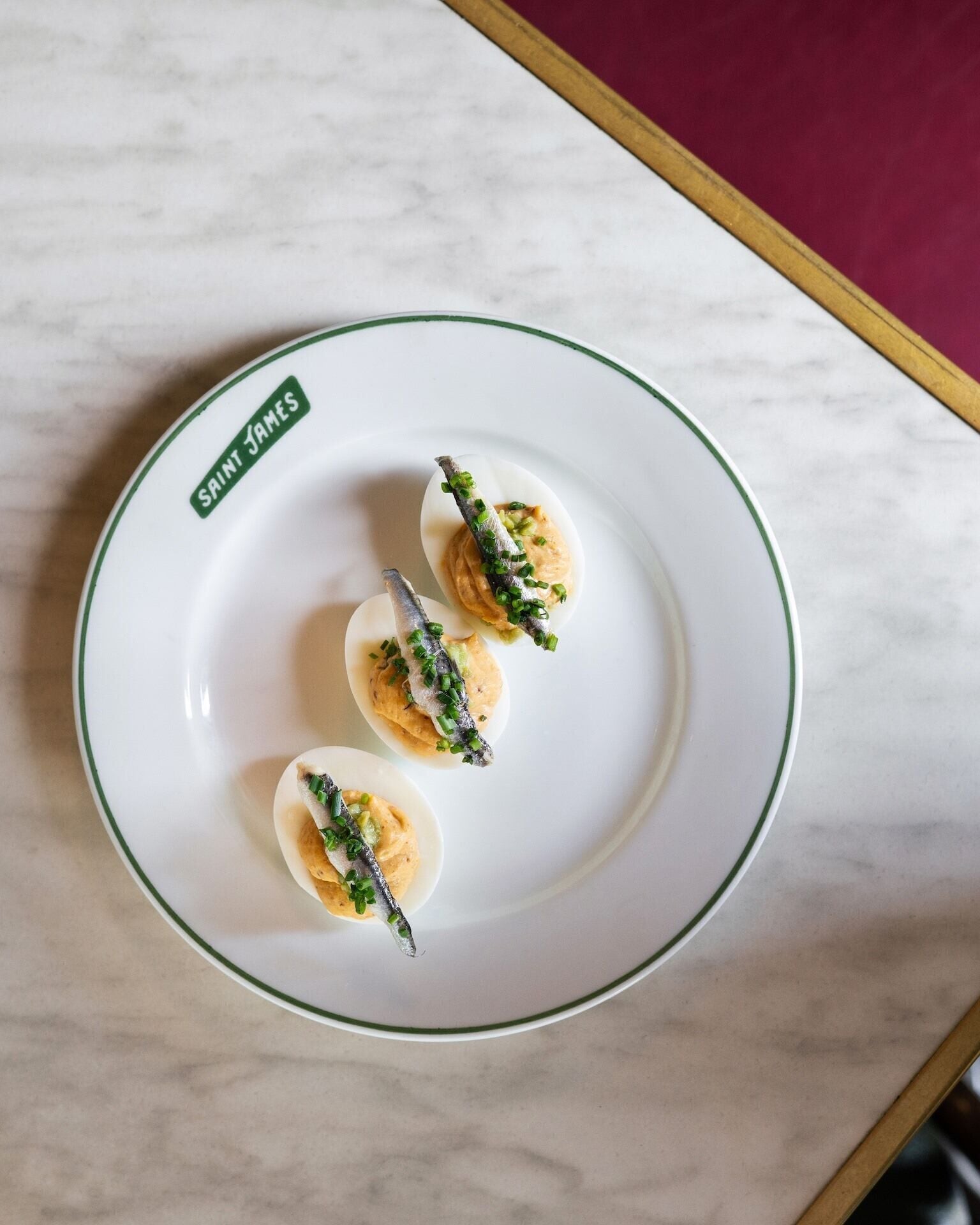 A plate with deviled eggs and anchovies on a white plate with a green rim.
