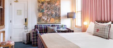 A hotel room with a large bed, a sofa, a small table, and a painting on the wall.