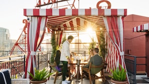 Una terraza en la azotea con toldo a rayas, plantas en macetas y vistas de la ciudad.