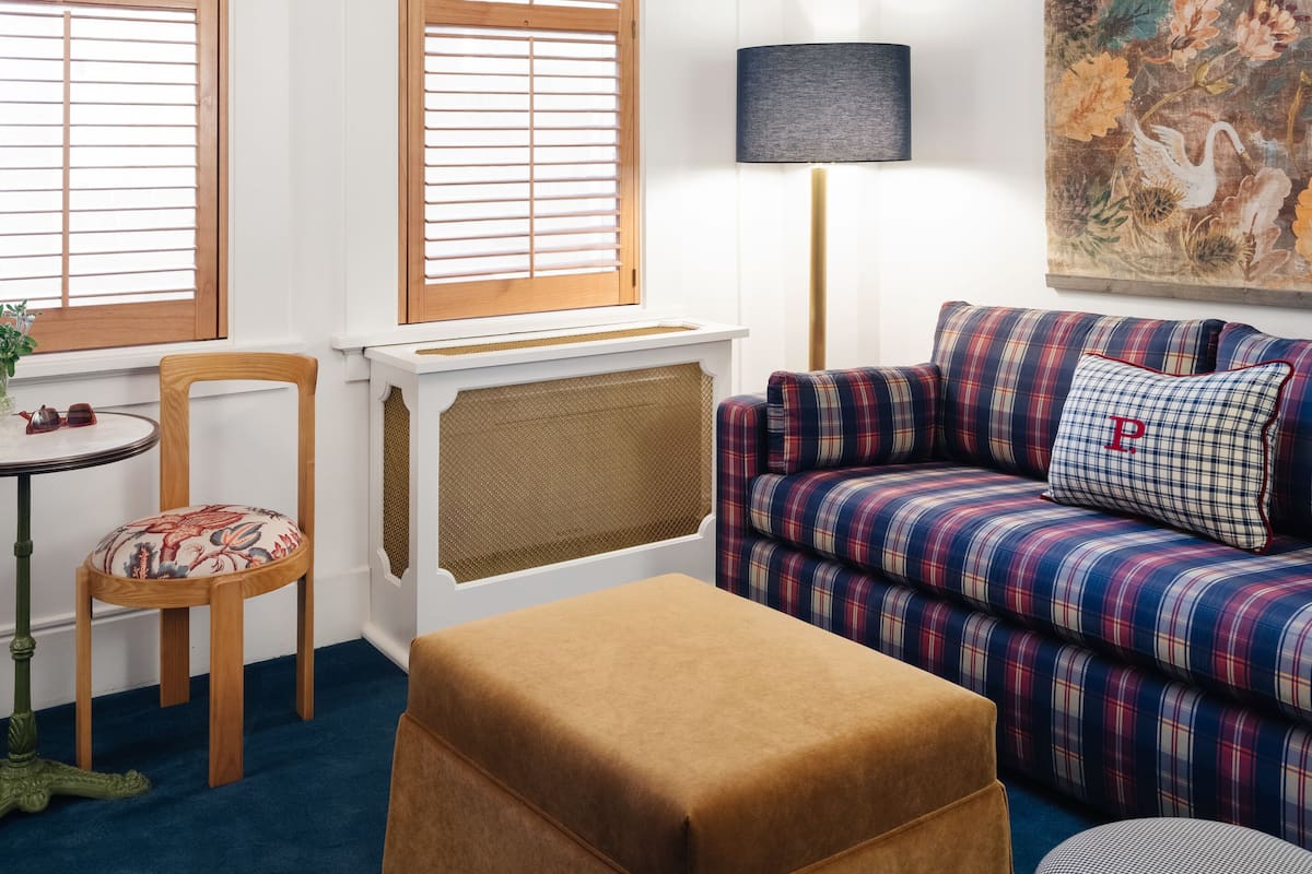 Ein Zimmer mit einer Couch, Hocker, Sessel und einem Tisch mit Lampe.