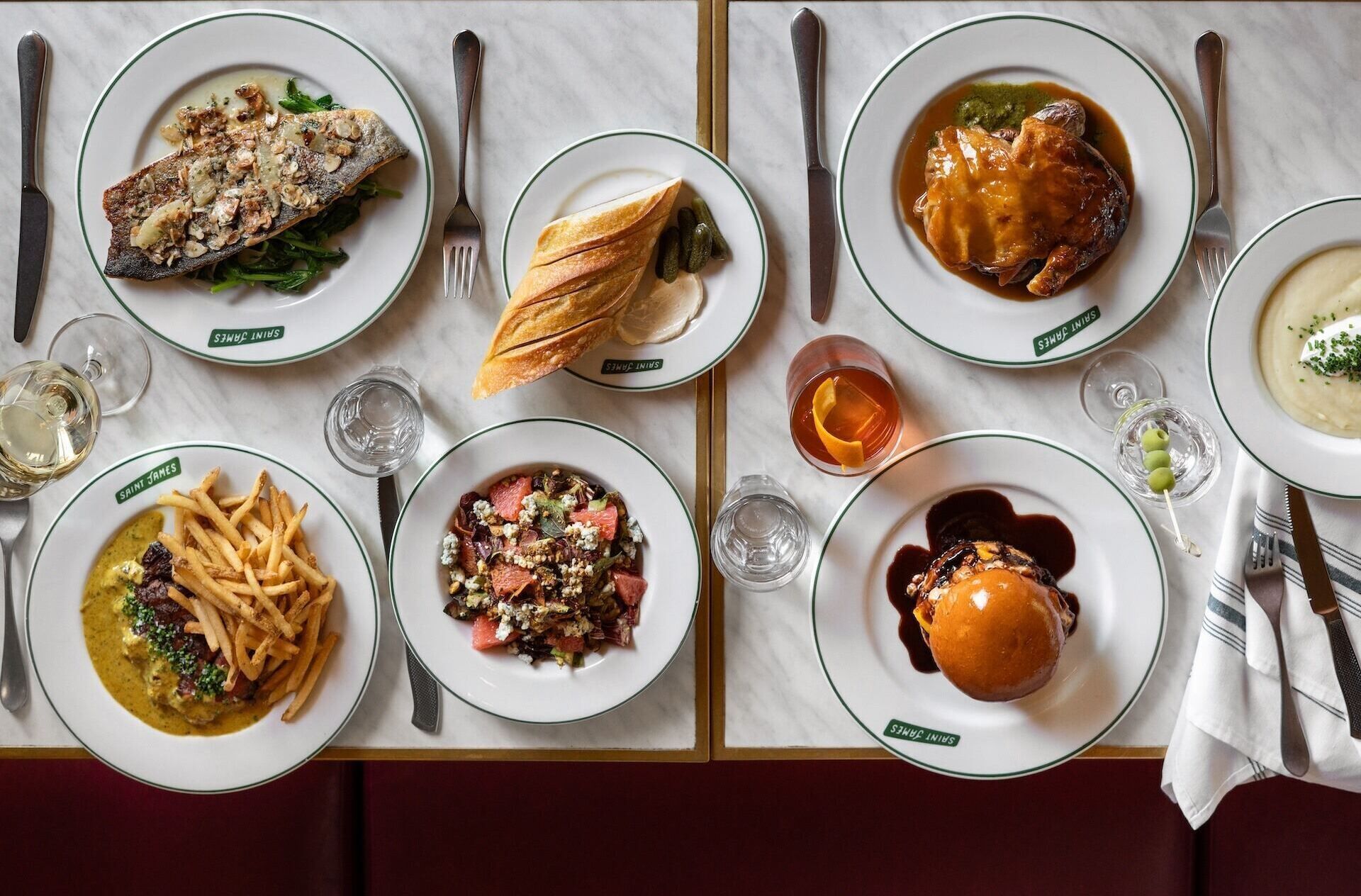 Une table dressée avec différents plats, couverts et verres, indiquant une mise en place pour le repas.