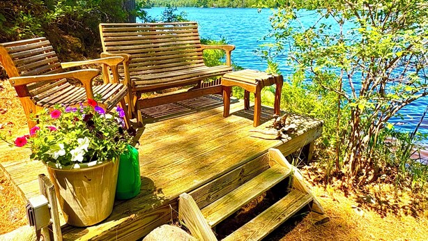 Une terrasse en bois avec des bancs et une table, donnant sur un lac.