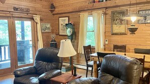 L’intérieur chaleureux d’un chalet avec des murs en bois, des fauteuils en cuir, une table à manger et une cheminée.