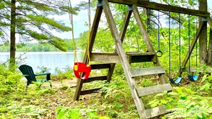 Une balançoire en bois, avec un banc et un siège de balançoire, entourée de verdure et offrant une vue sur un lac.