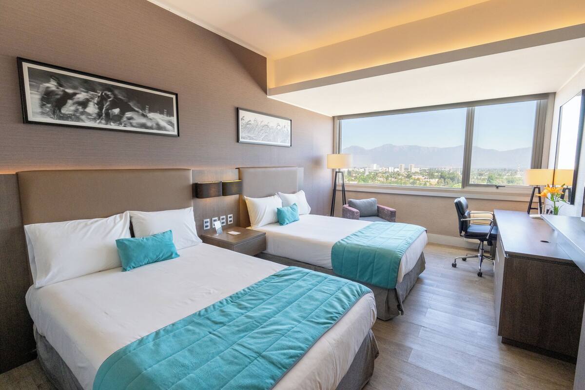 Habitación de hotel con dos camas, un escritorio y vistas a la ciudad.