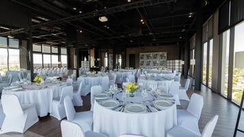 A large indoor dining area with round tables, white chairs, and large windows.
