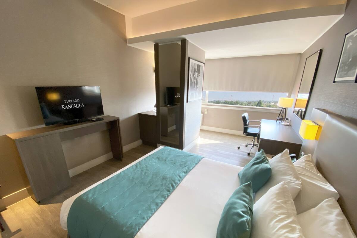 Habitación de hotel con cama, televisión, escritorio y balcón con vistas.