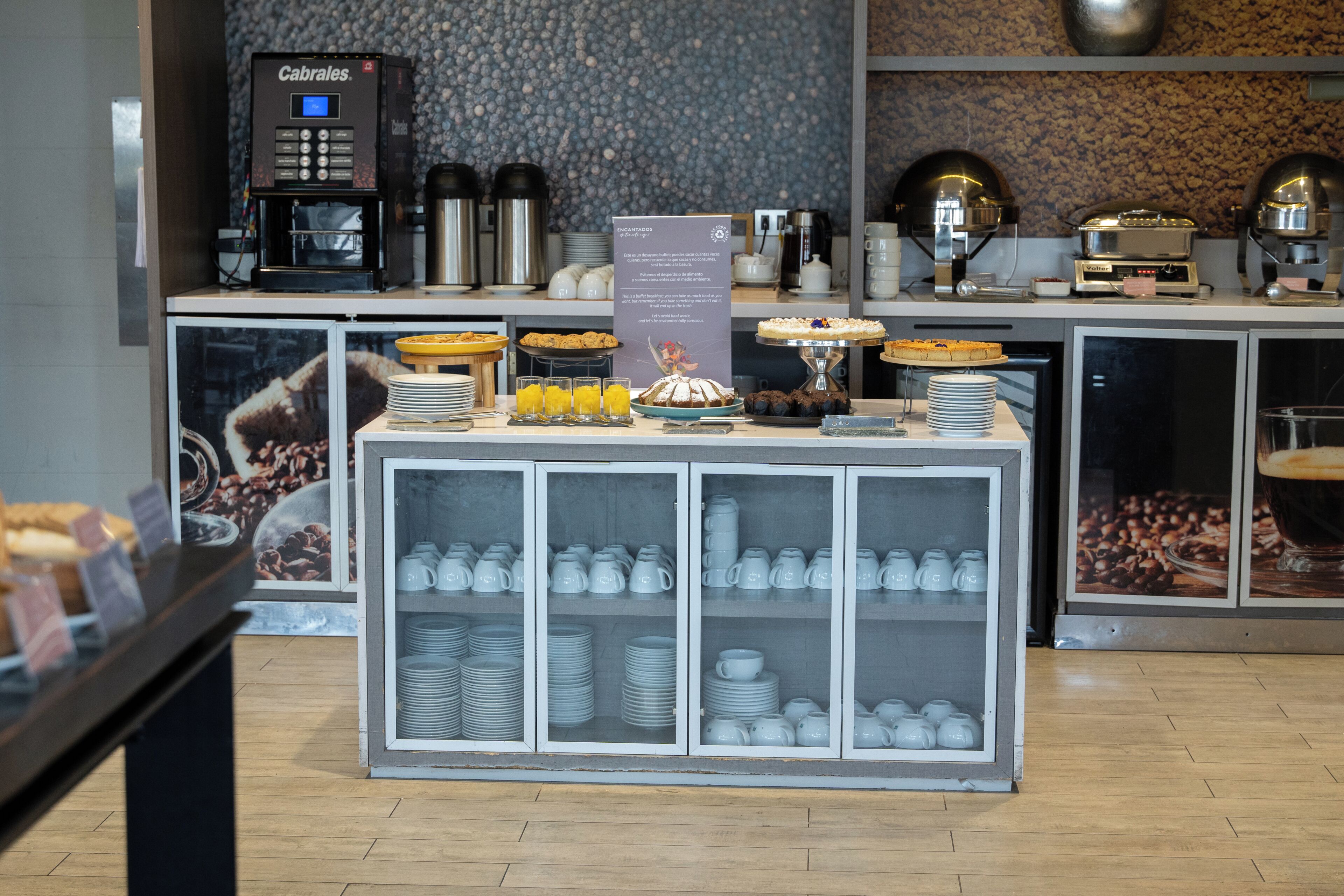 Un bufé de desayuno con diferentes opciones de comida, una máquina de café y una exhibición de tazas y vasos.