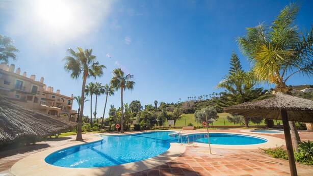 A swimming pool area with multiple pools, palm trees, and a building with balconies in the background. - La Almadraba apartment 204 (Manilva)