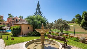 A courtyard with a fountain, a pool, and a golf course in the background. - La Almadraba apartment 204 (Manilva)