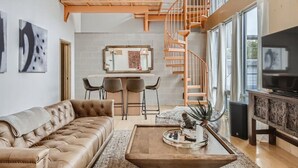 A spacious living area with a high ceiling, a wooden staircase, a comfortable sofa, a dining table with chairs, and a television on a cabinet. - Spacious Retreat for Groups W/Workspace Min to DT & SXSW Top Spots! (Austin)