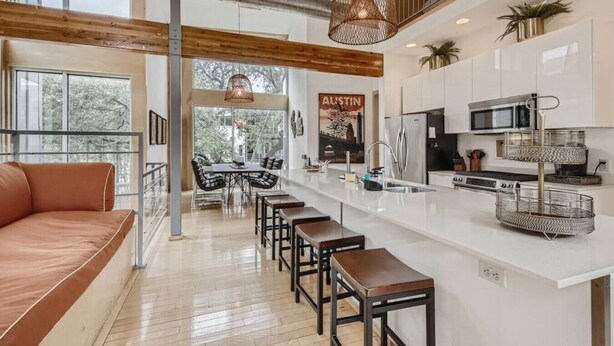 A modern kitchen with a central island, stainless steel appliances, and a dining area with a view of trees. - Spacious Retreat for Groups W/Workspace Min to DT & SXSW Top Spots! (Austin)