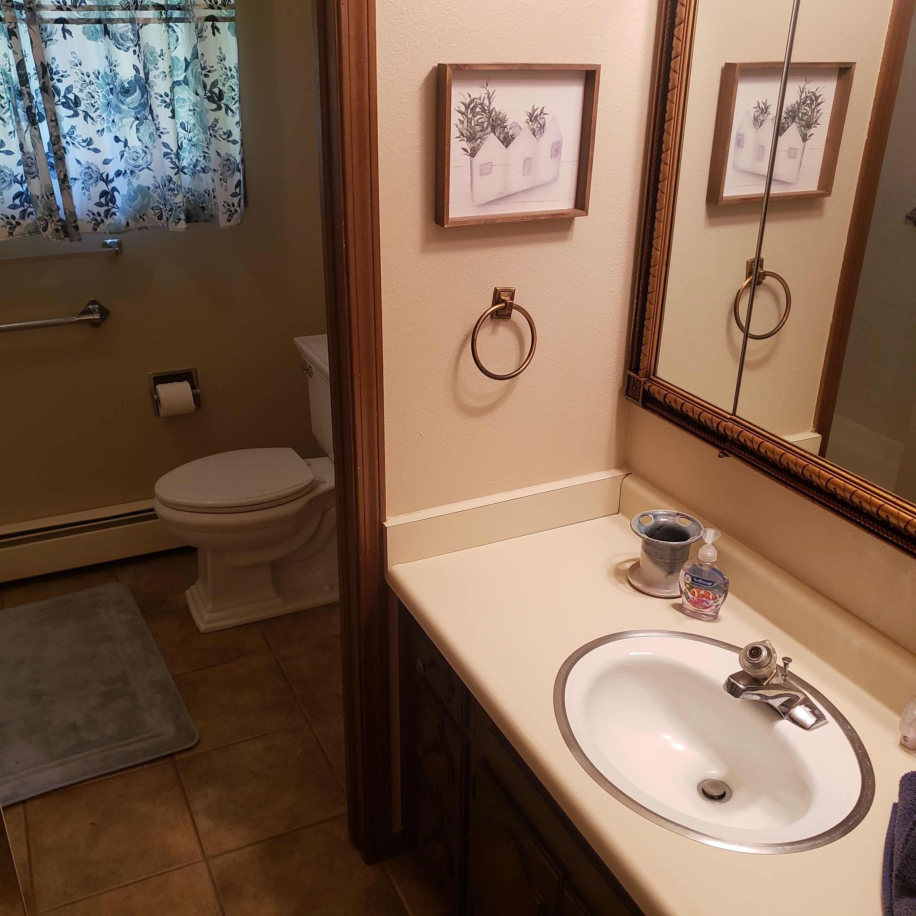 A bathroom with a toilet, sink, and a mirror. There are framed pictures on the wall and a towel rack.
