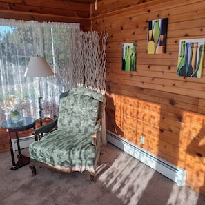 Una habitación acogedora con un sillón estampado, una mesita con lámpara y decoración en las paredes.