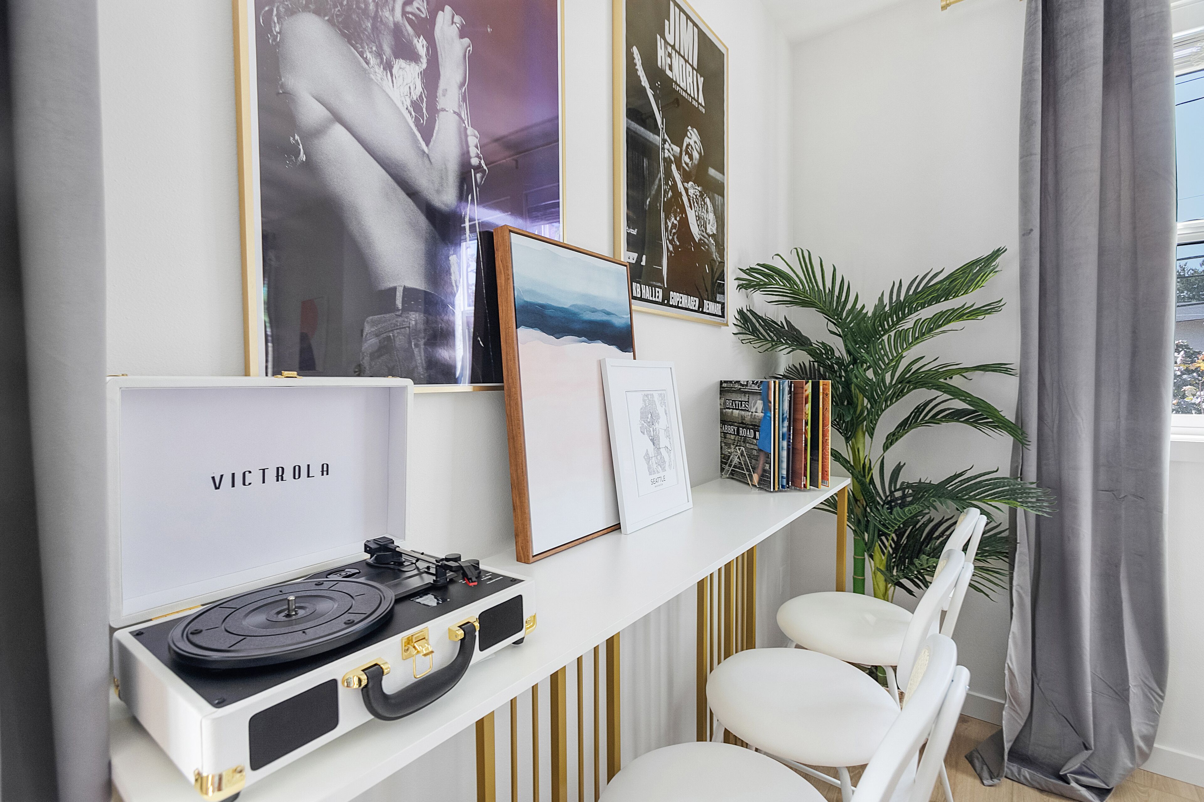 Una habitación con un escritorio blanco, un tocadiscos, cuadros enmarcados, una estantería y una planta en maceta.