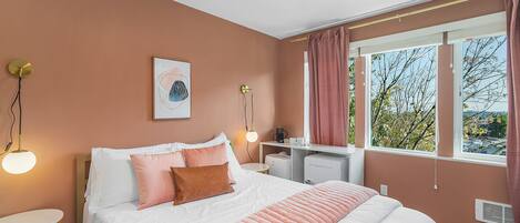 Un dormitorio con cama, mesitas de noche, escritorio y ventana con cortinas.