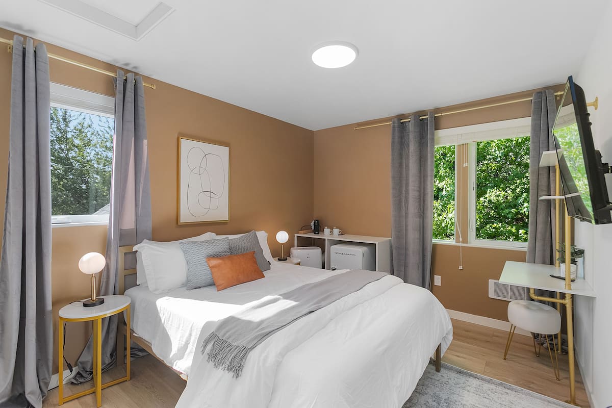 A bedroom with a bed, bedside table, lamp, and a desk with a chair.