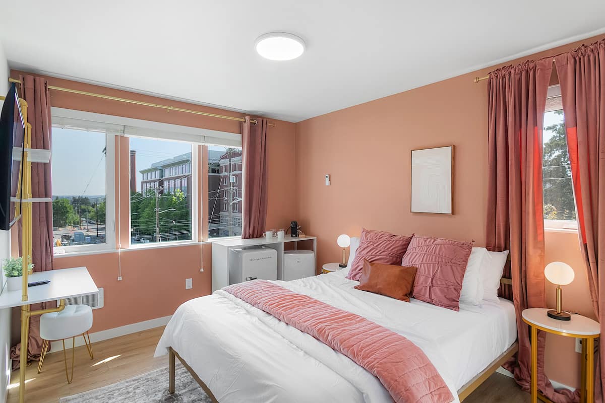 A modern bedroom with a bed, bedside tables, a desk, and a window with curtains.